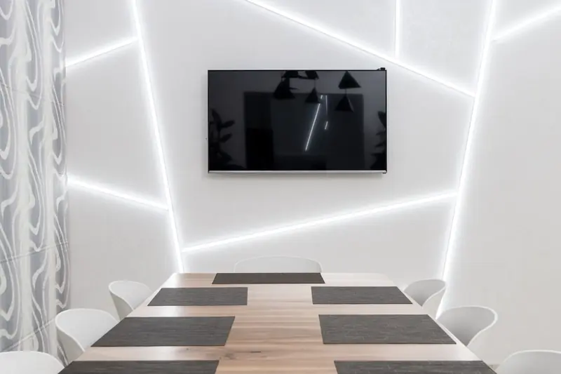 Geometric lamps and television with black screen against chairs and table with placemats in light house
