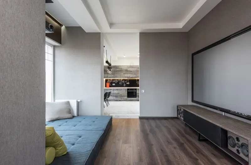 Blue mattress with cushions placed against wall with contemporary big TV in stylish modern light apartment with kitchen zone and creative design