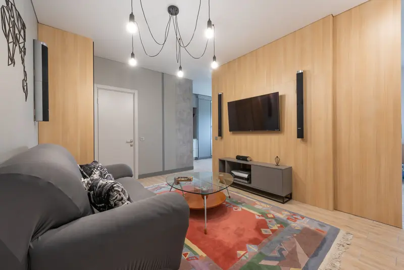 Modern apartment Interior with sofa with pillows near glass table on carpet near cabinet and TV with speakers near lamp on ceiling and door