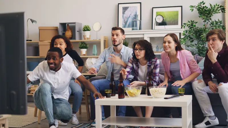 A diverse group of friends excitedly watching TV together in a modern living room setting