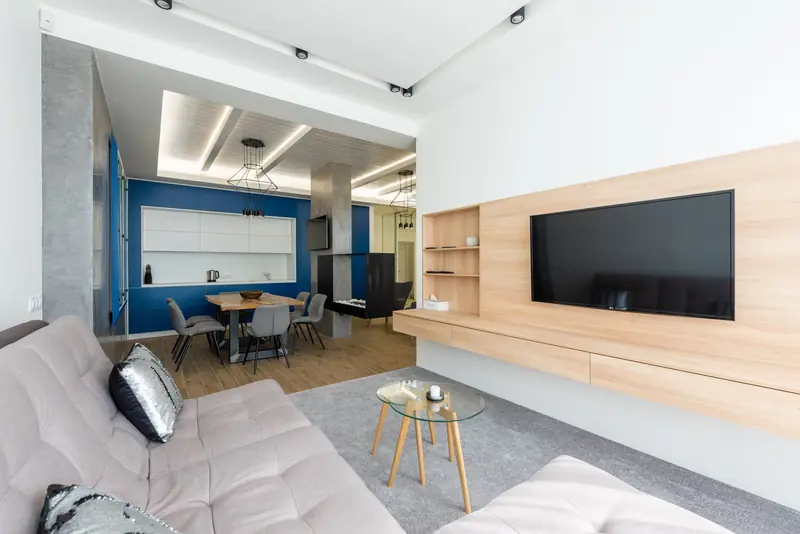 Interior of modern studio apartment with TV set hanging opposite sofa in living room and comfortable kitchen under luminous lights