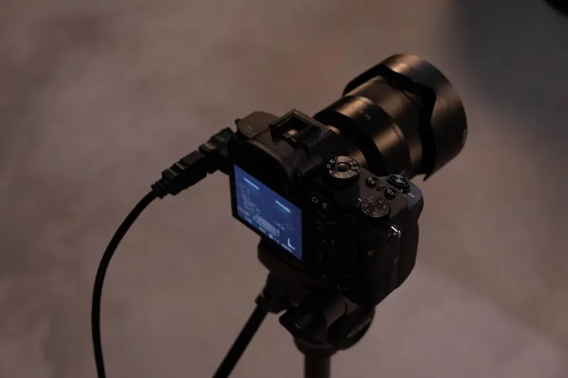 Detailed view of a professional camera setup on a tripod indoors, showcasing its screen and cables