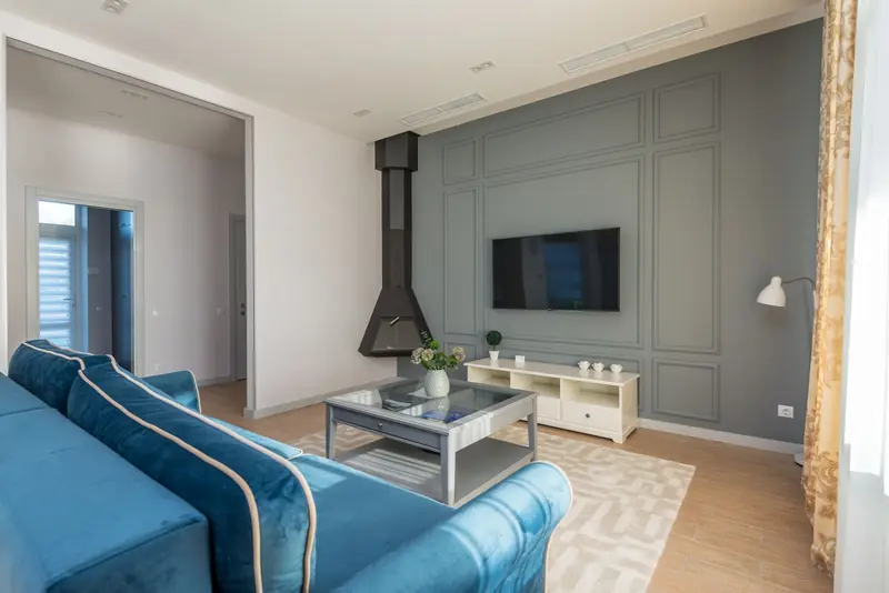 A stylish living room featuring a blue couch, wall-mounted TV, and elegant decor