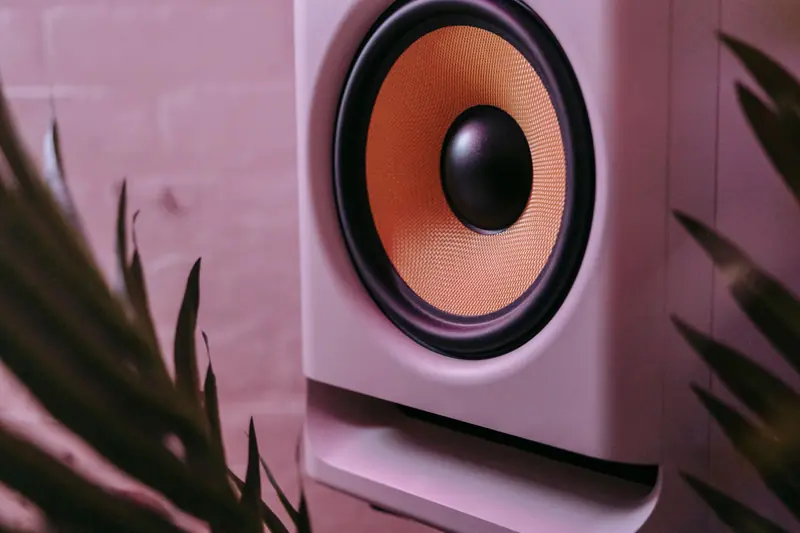 Close-up photo of a stylish subwoofer surrounded by foliage and ambient lighting