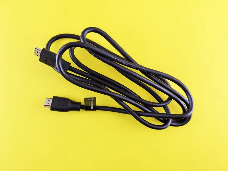 A neatly coiled black HDMI cable displayed on a vibrant yellow surface, ideal for tech visuals